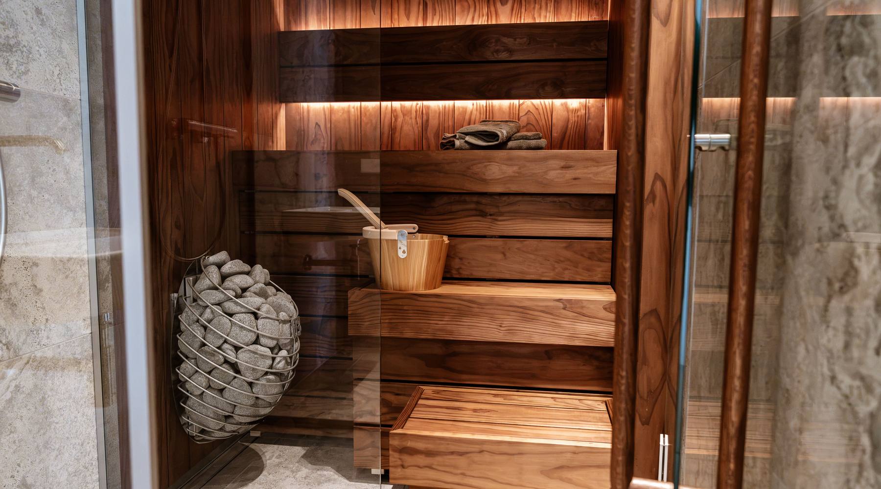A glass-fronted indoor sauna with lit cedar benches and a stone heater